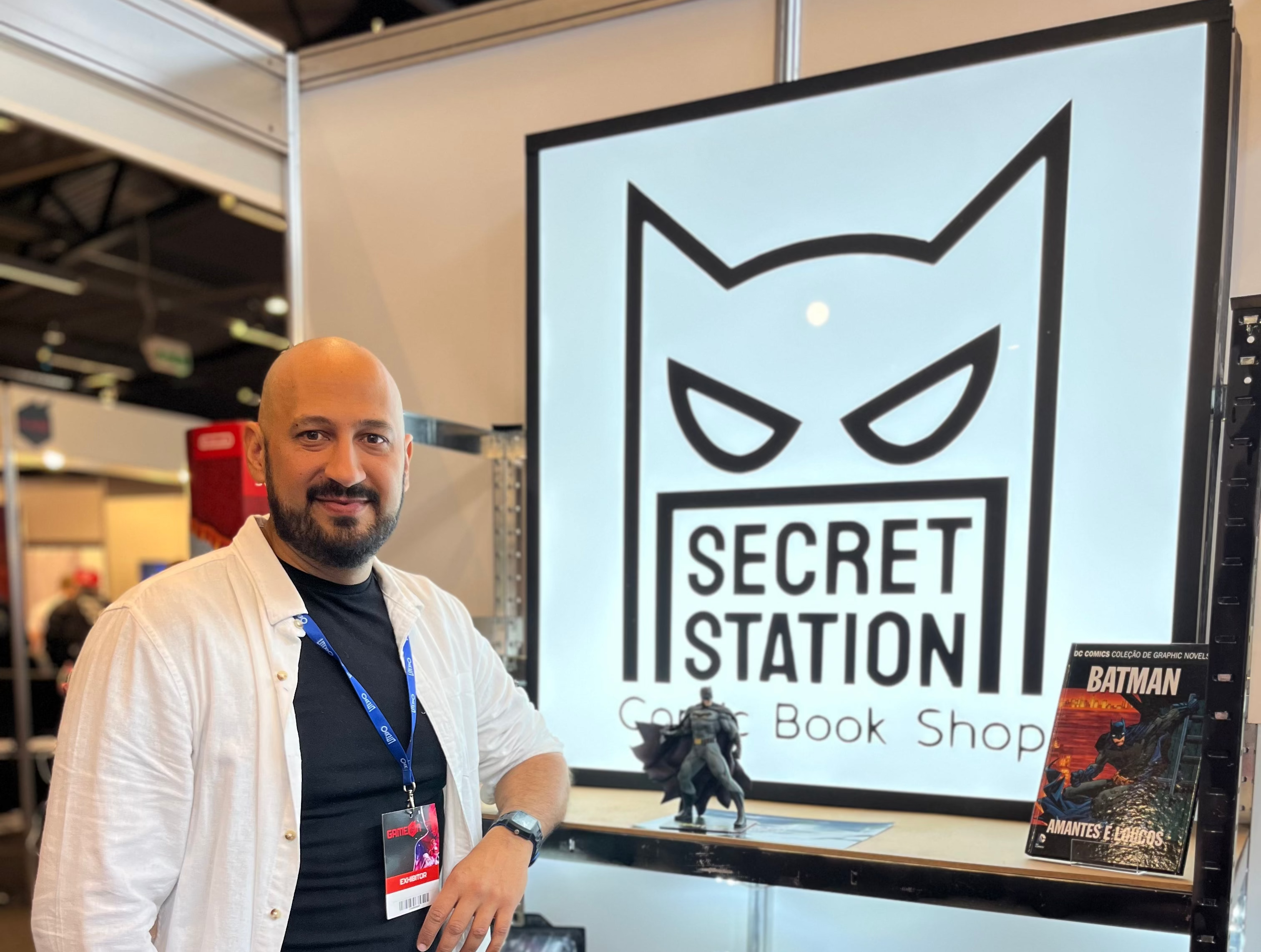 Man standing in front of a Secret Station comic book shop display with superhero figurines and merchandise.